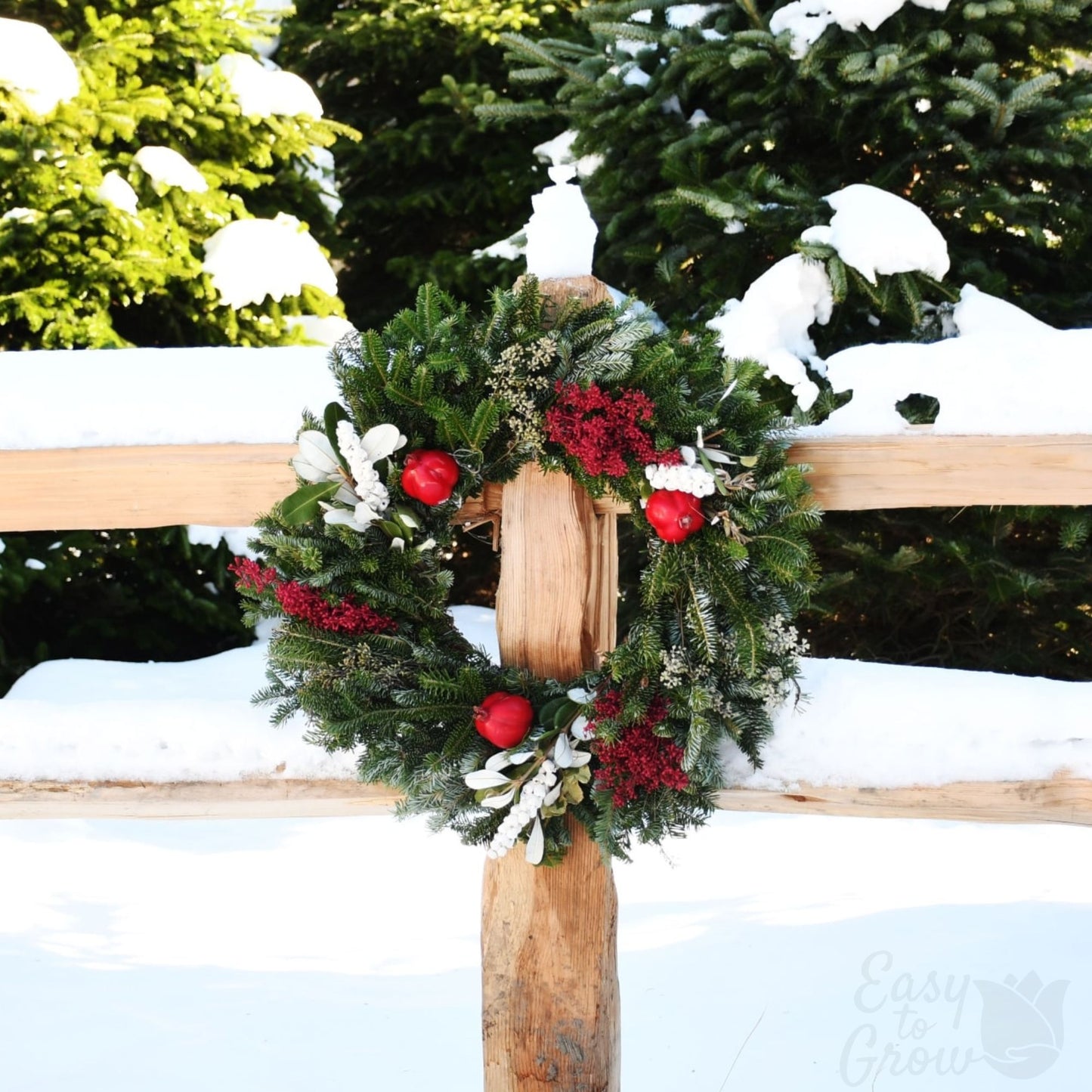 Winter Orchard luxe wreath on a fence post featuring green and white foliage and red accents.