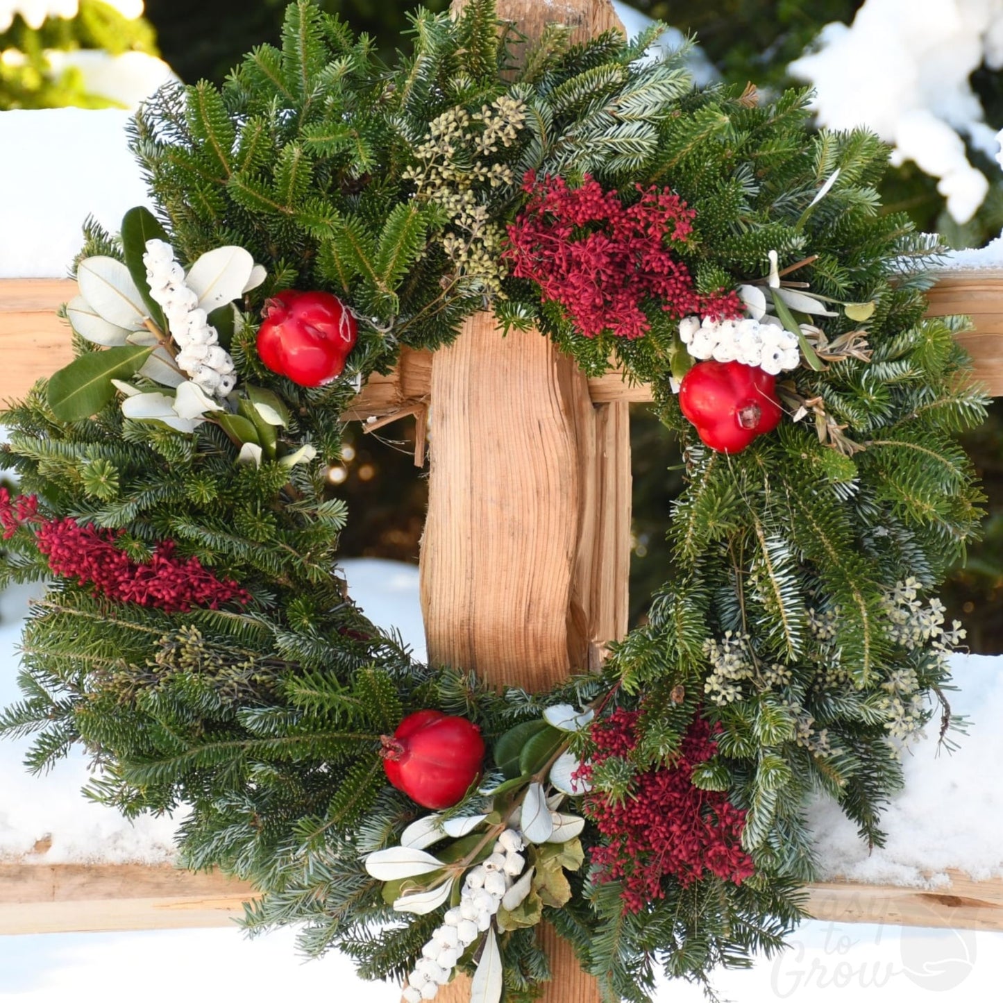 Winter Orchard luxe wreath close up on a fence post featuring green and white foliage and red accents.